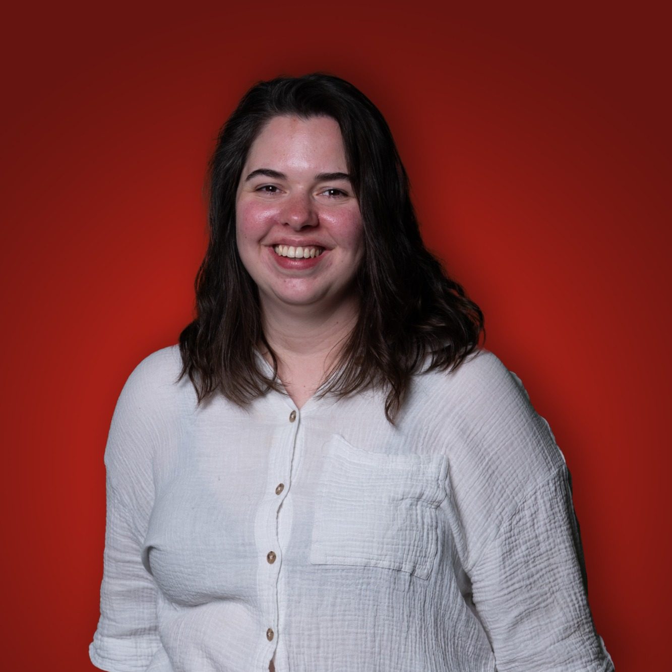 Jonge vrouw met lange, golvende haren, lachend tegen een rode achtergrond.