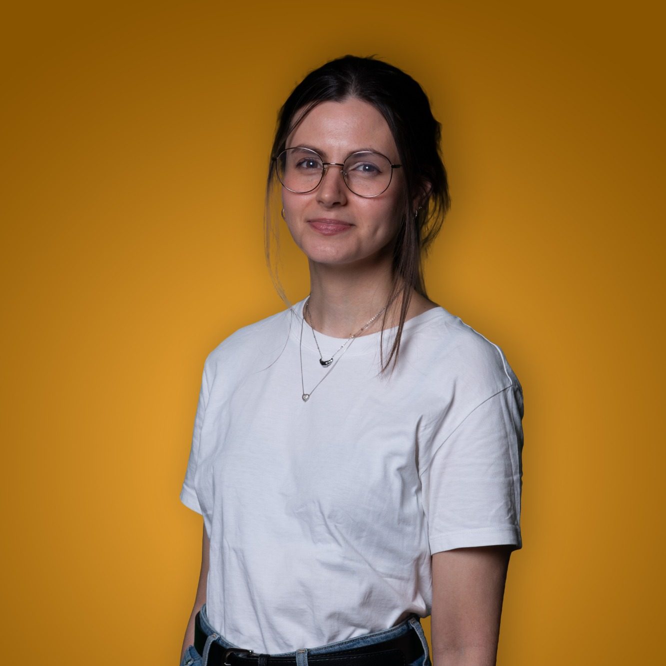 Vrouw met een bril en een witte T-shirt voor een gele achtergrond.