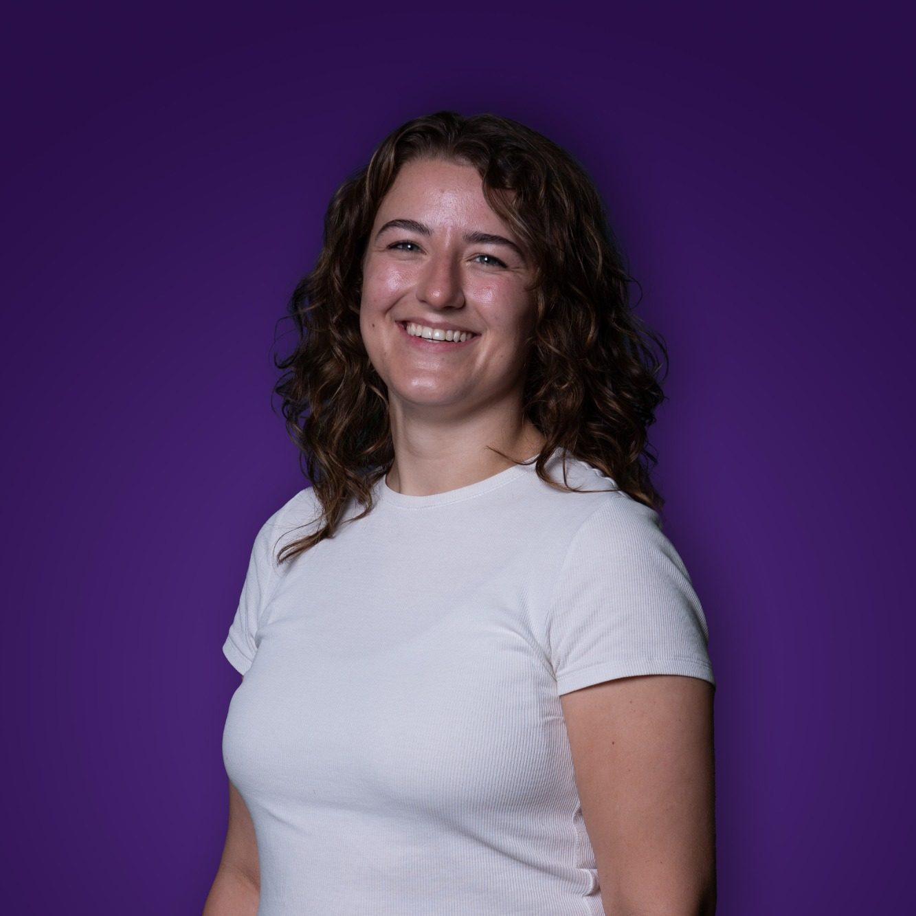 Vrouw met krullend haar, glimlachend op een paarse achtergrond.